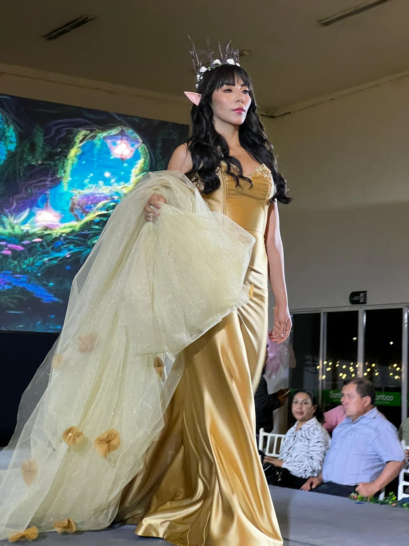 Diseño dorado de ARCADIA con capa de tul marfil, presentado en pasarela.